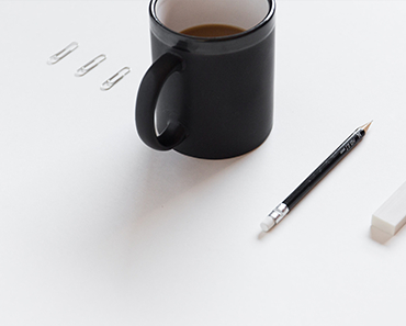 A black mug of coffee beside paper clips and a pencil