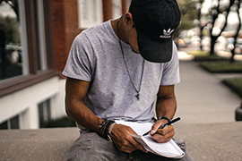 a person is sitting on a ledge writing in a notebook